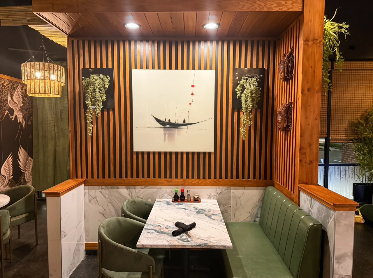An intimate olive-green booth with marble table and boat artwork on a wooden slat wall.