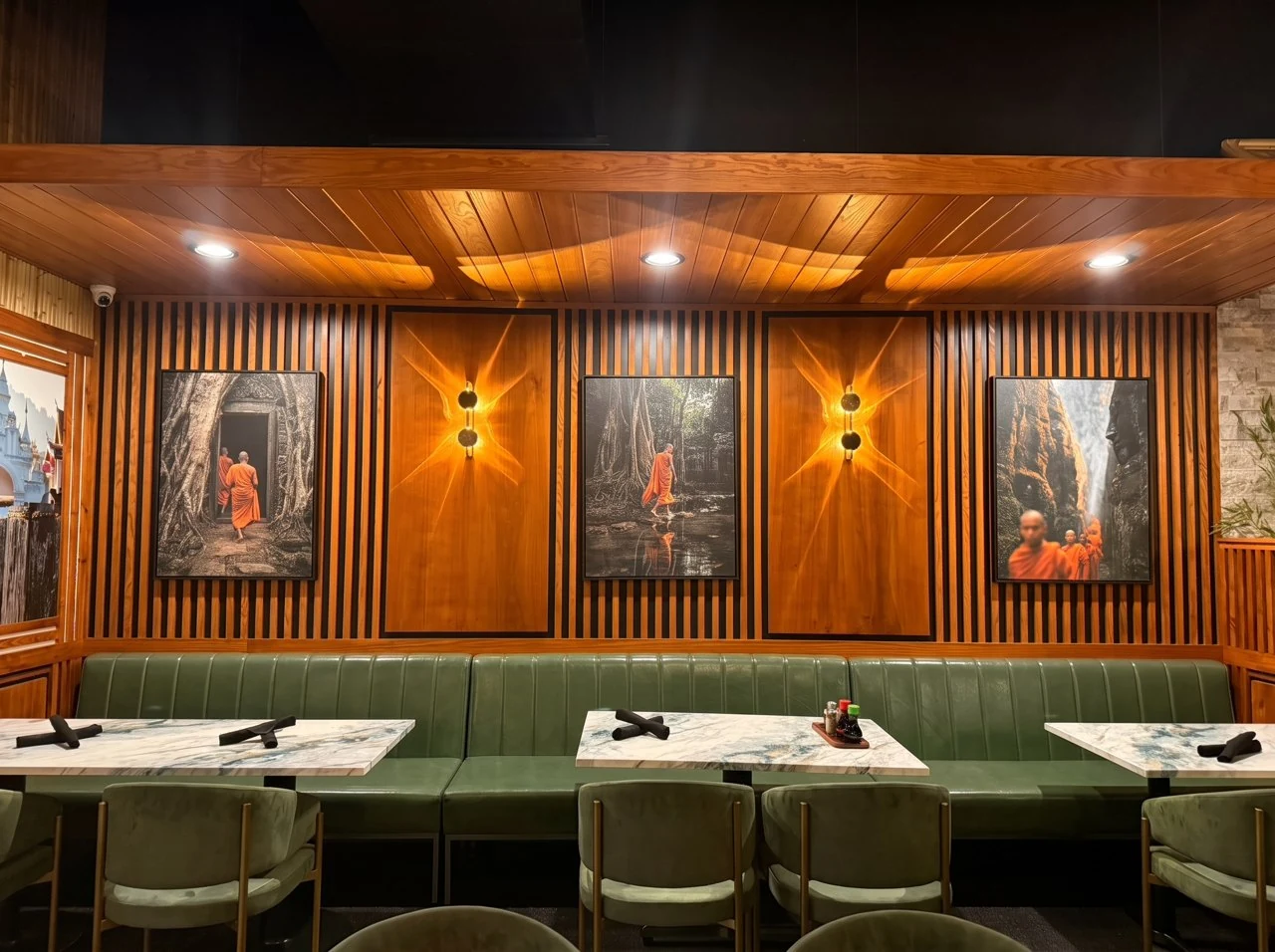 Olive-green banquette seating beneath three framed artworks and warm wall sconces at Thai Zen.