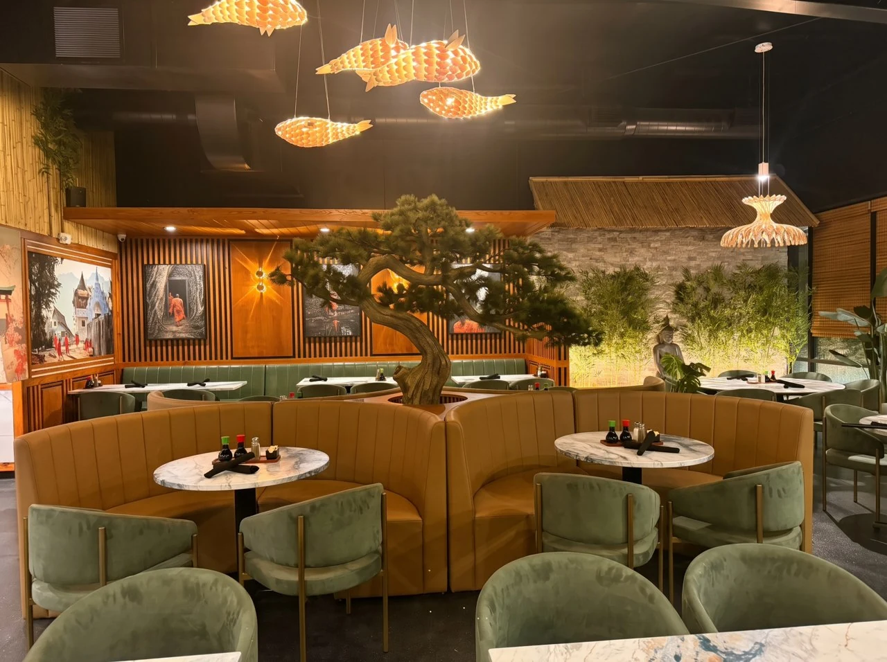 Thai Zen dining room with a central bonsai tree, round golden booths and fish-shaped pendant lights.