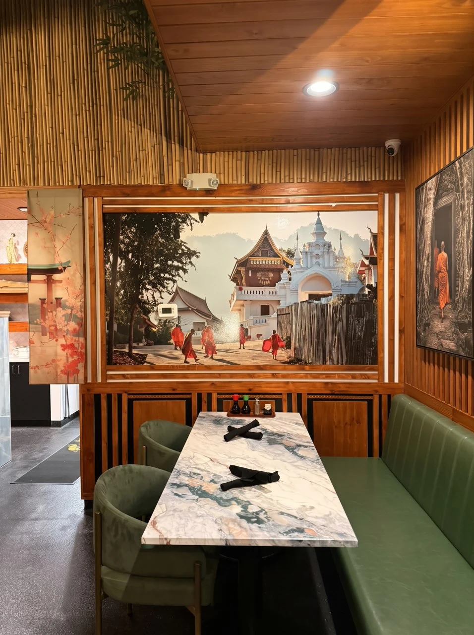 A green upholstered booth beside a framed temple mural and warm bamboo paneling.